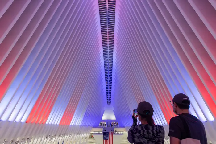 Silhouettes of two people admiring the Oculus's "ribbed" roof which is lit up in red white and blue for Veterans Day